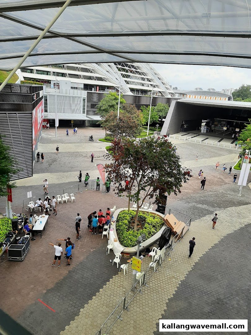 An aerial view of a modern outdoor plaza with people, trees, and contemporary buildings under a translucent roof.