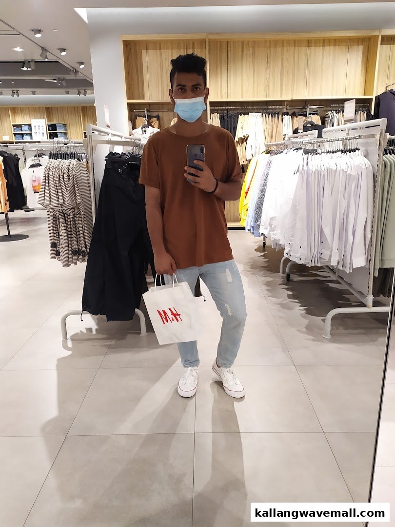 A person wearing a mask holds an H&M shopping bag inside a brightly lit clothing store.