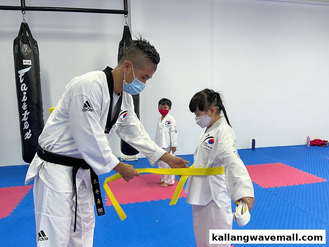 An instructor helps a child tie a yellow belt during a Taekwondo class at HAN Taekwondo.