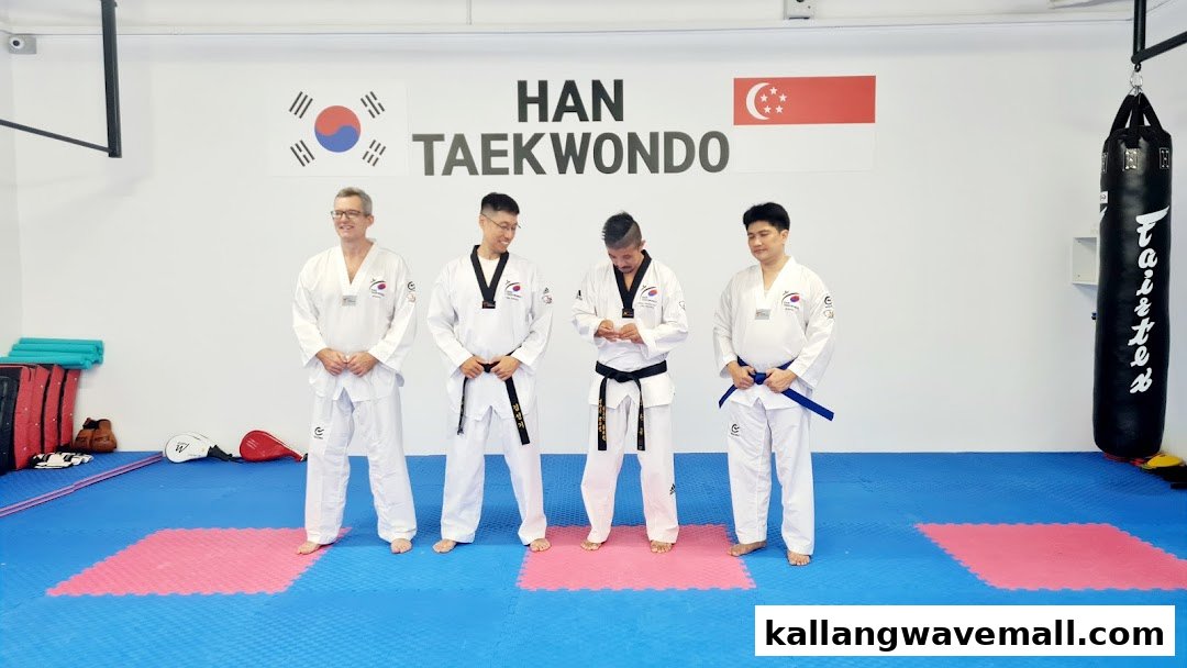 Four individuals in Taekwondo uniforms stand in a bright studio with flags and training equipment.