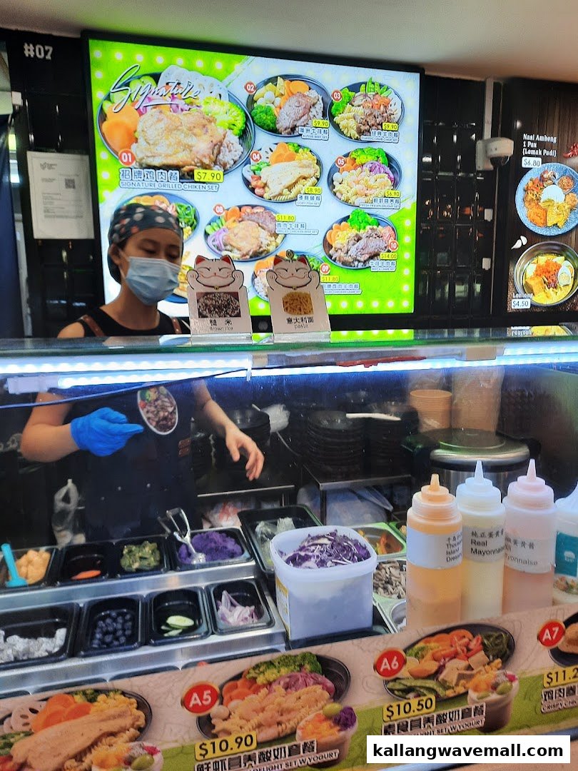 A staff member prepares fresh ingredients at a healthy food stall with vibrant menu displays.