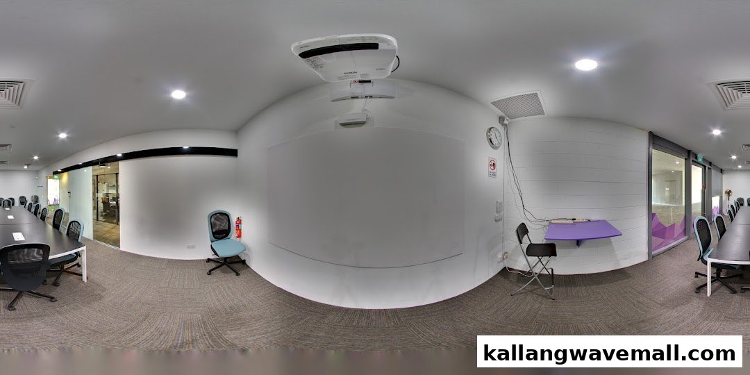 A modern, well-lit conference or classroom space with a large table, chairs, projector, and whiteboard.