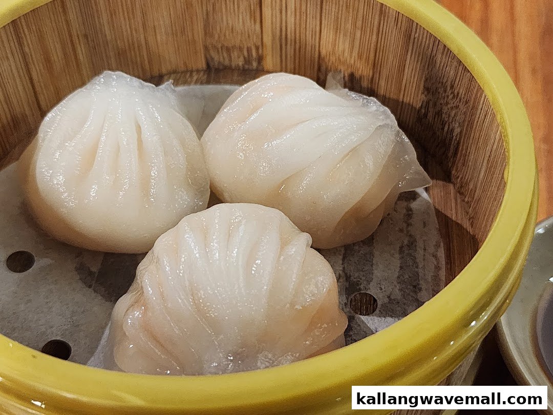 Three translucent steamed dumplings, likely har gow, served in a traditional bamboo steamer.