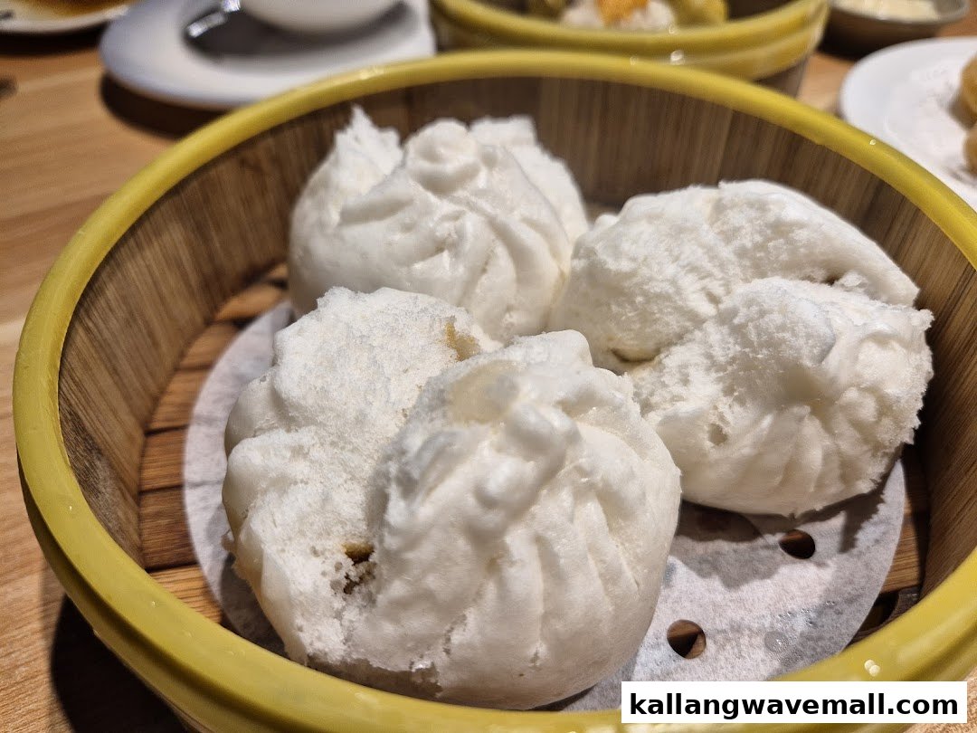 Four fluffy white dim sum buns in a yellow-rimmed bamboo steamer.
