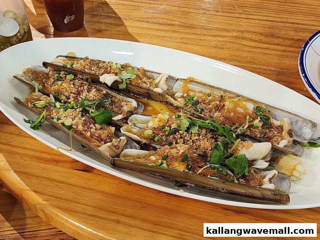A white platter of steamed razor clams with vermicelli, garlic, and herbs on a wooden table.