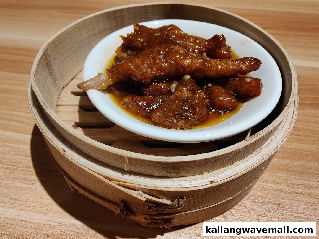 A close-up of braised chicken feet served in a white dish inside a traditional bamboo steamer.
