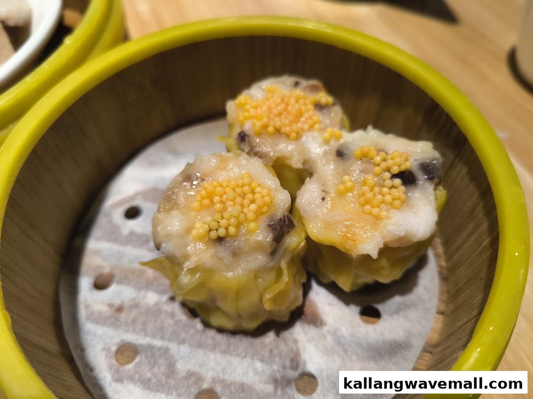 Close-up of three steamed siu mai dumplings topped with fish roe in a bamboo steamer.
