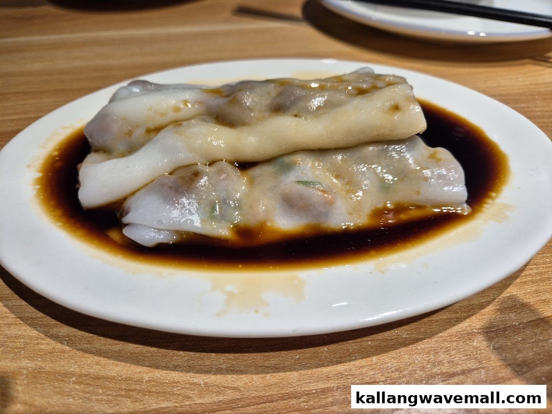 A close-up of two rice noodle rolls (Cheung Fun) with savory sauce on a white plate.