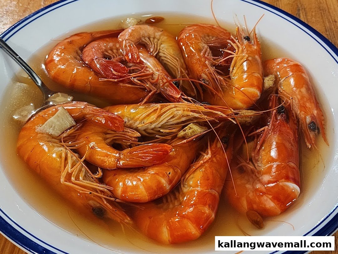 A close-up of a bowl filled with vibrant orange cooked shrimp in a clear broth, with a spoon.