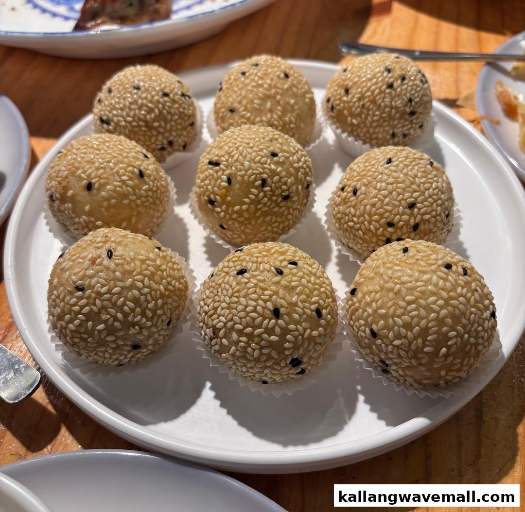 A white plate filled with nine golden-brown sesame balls, sprinkled with black and white sesame seeds.
