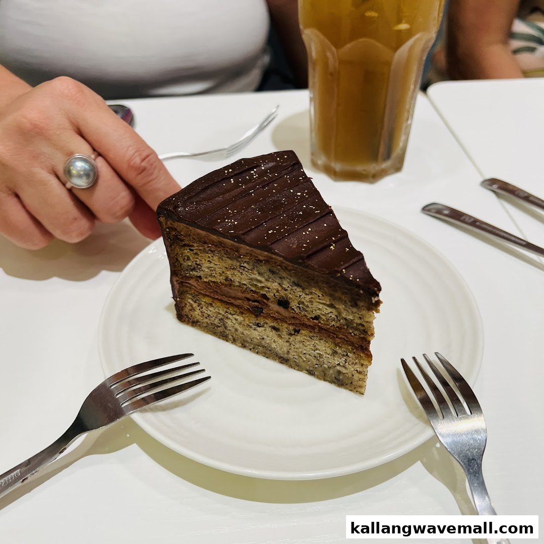 A delicious slice of chocolate-frosted cake with a layered filling, served on a white plate with forks and a drink.
