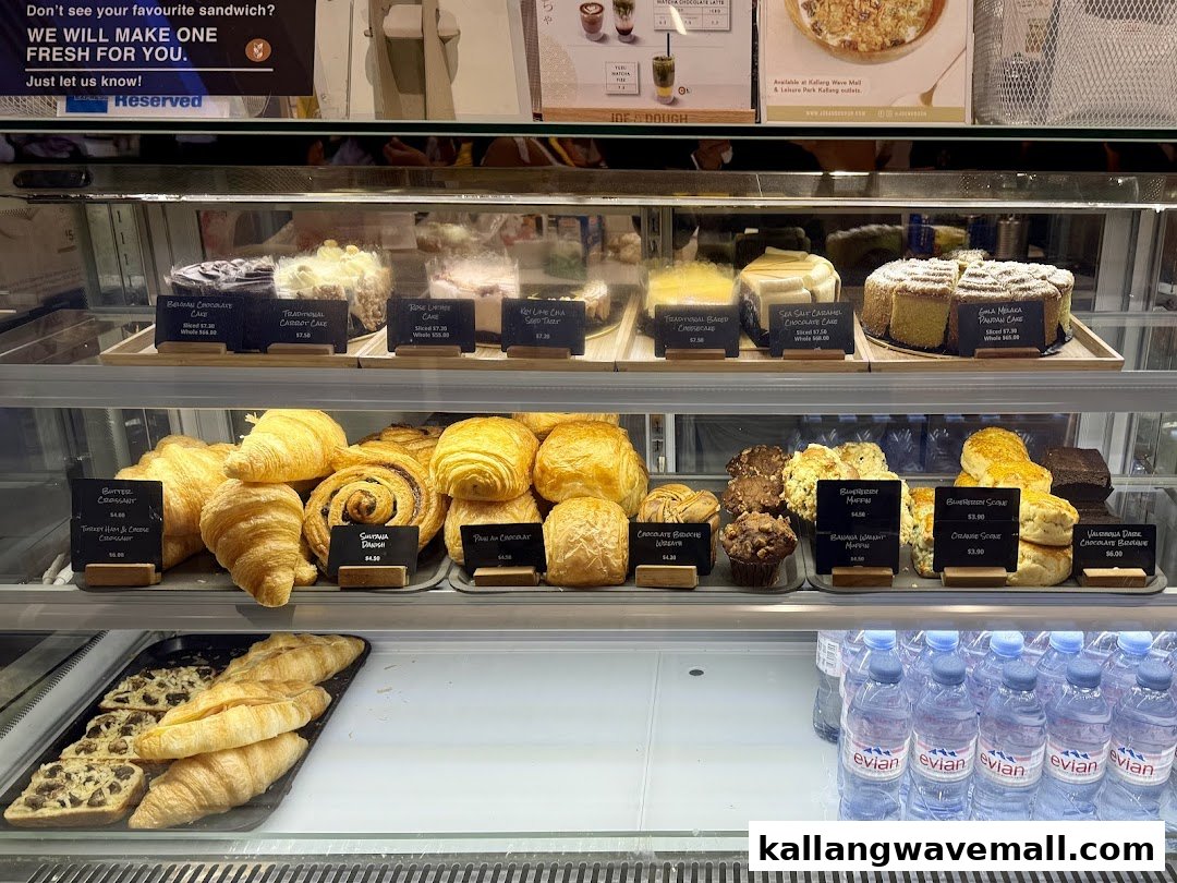 A vibrant display case showcasing a variety of freshly baked cakes, pastries, muffins, and bottled water.