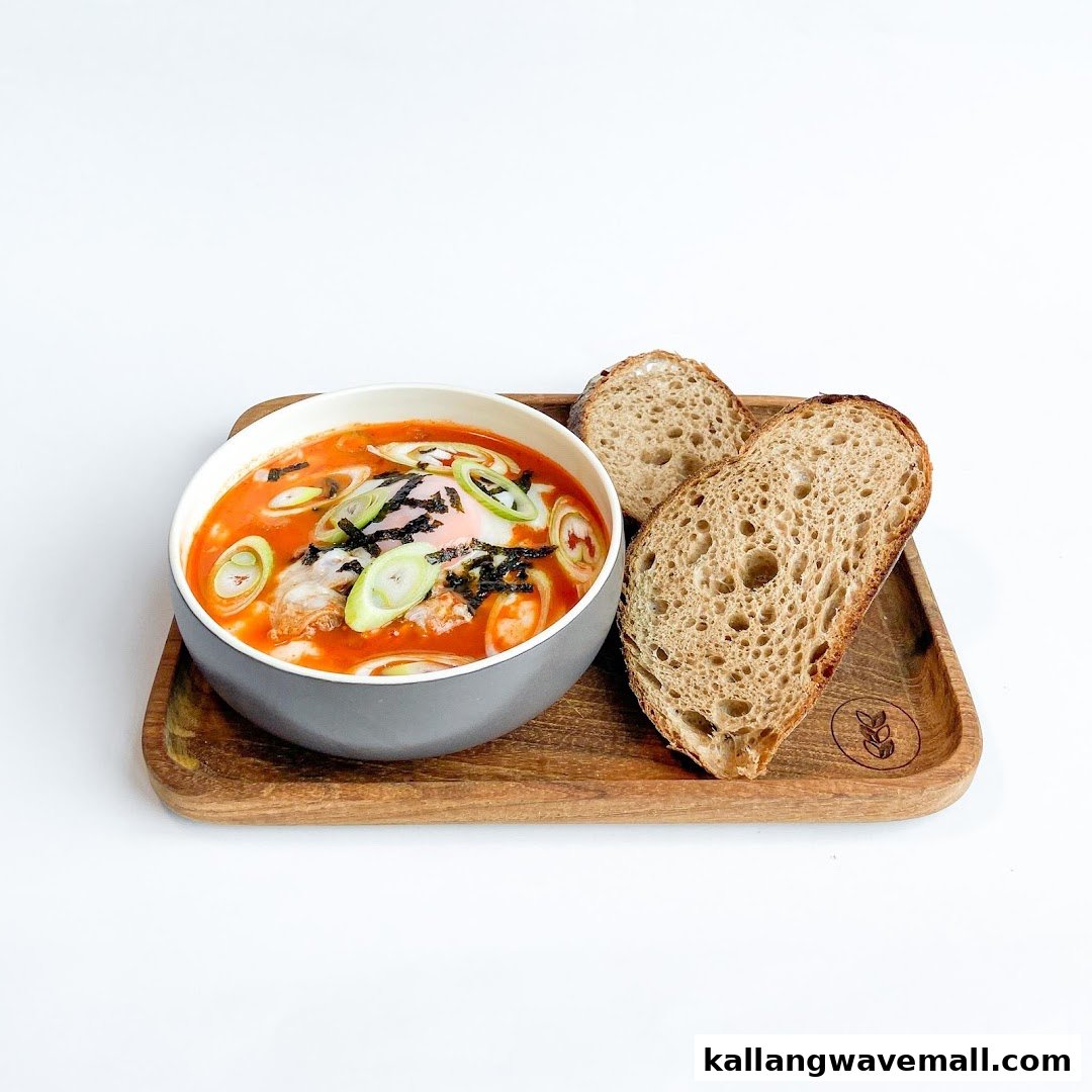 A vibrant bowl of soup with a poached egg, spring onions, and seaweed, served with sourdough bread on a wooden tray.