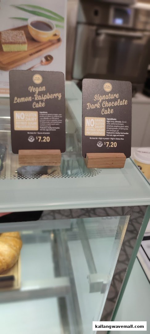 Two display signs for 'Oh My Goodness!' vegan lemon-raspberry and signature dark chocolate cakes with prices.