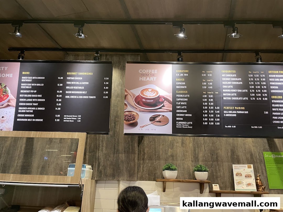 Two large digital menu boards displaying a variety of food and coffee options inside Joe & Dough.