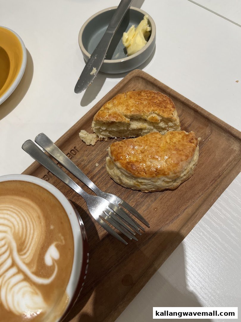 A close-up of golden pastries and a latte with latte art on a wooden board, served with butter.