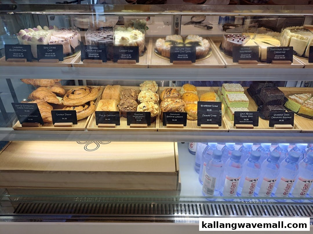 A vibrant display case showcasing a variety of freshly baked cakes, pastries, and bottled water.