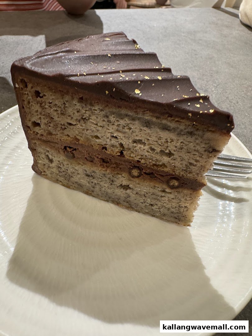 A delicious slice of chocolate-frosted cake with gold flakes on a white plate.
