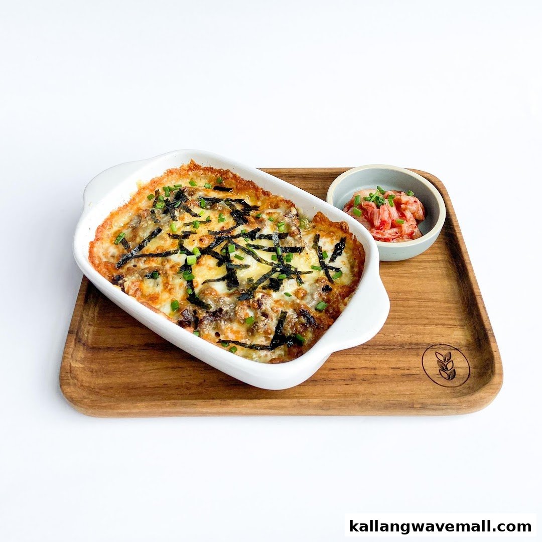 A baked dish topped with cheese, seaweed, and green onions, served with kimchi on a wooden tray.