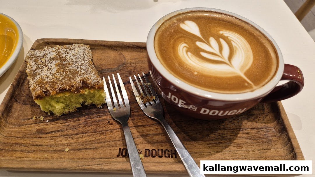 A coffee latte with intricate latte art and a slice of cake on a wooden serving tray.