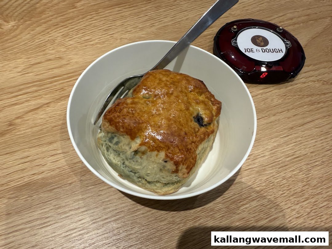 A golden-brown scone in a white bowl with a fork, next to a Joe & Dough buzzer.