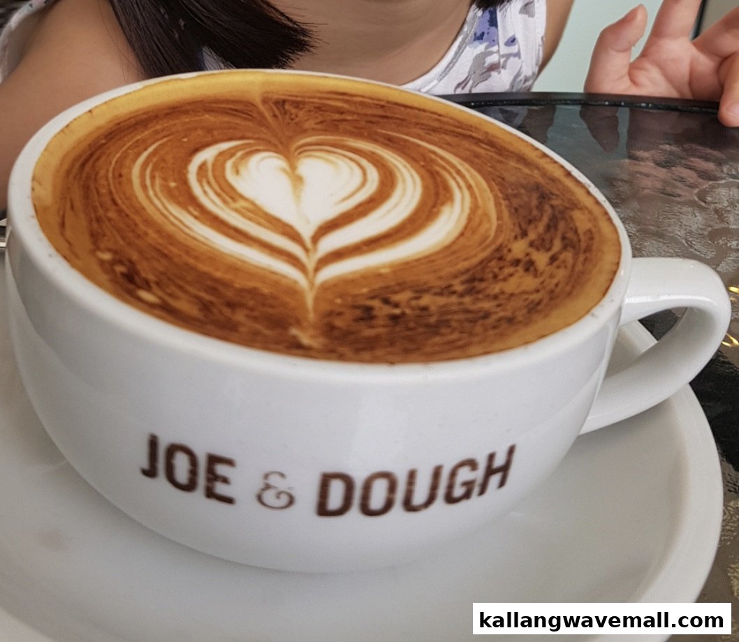 A close-up of a latte with heart-shaped latte art in a white Joe & Dough cup.