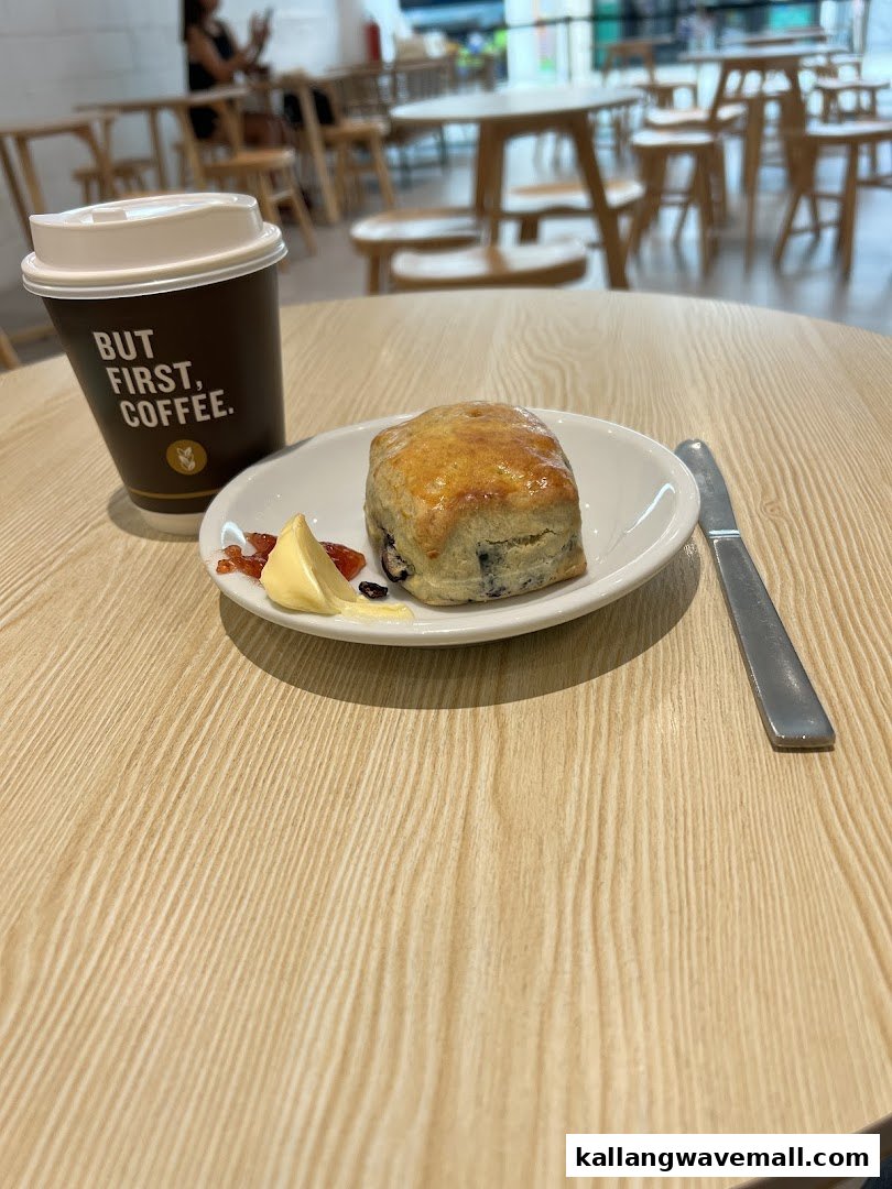 A delicious scone with jam and butter, alongside a coffee cup, on a light wooden table.
