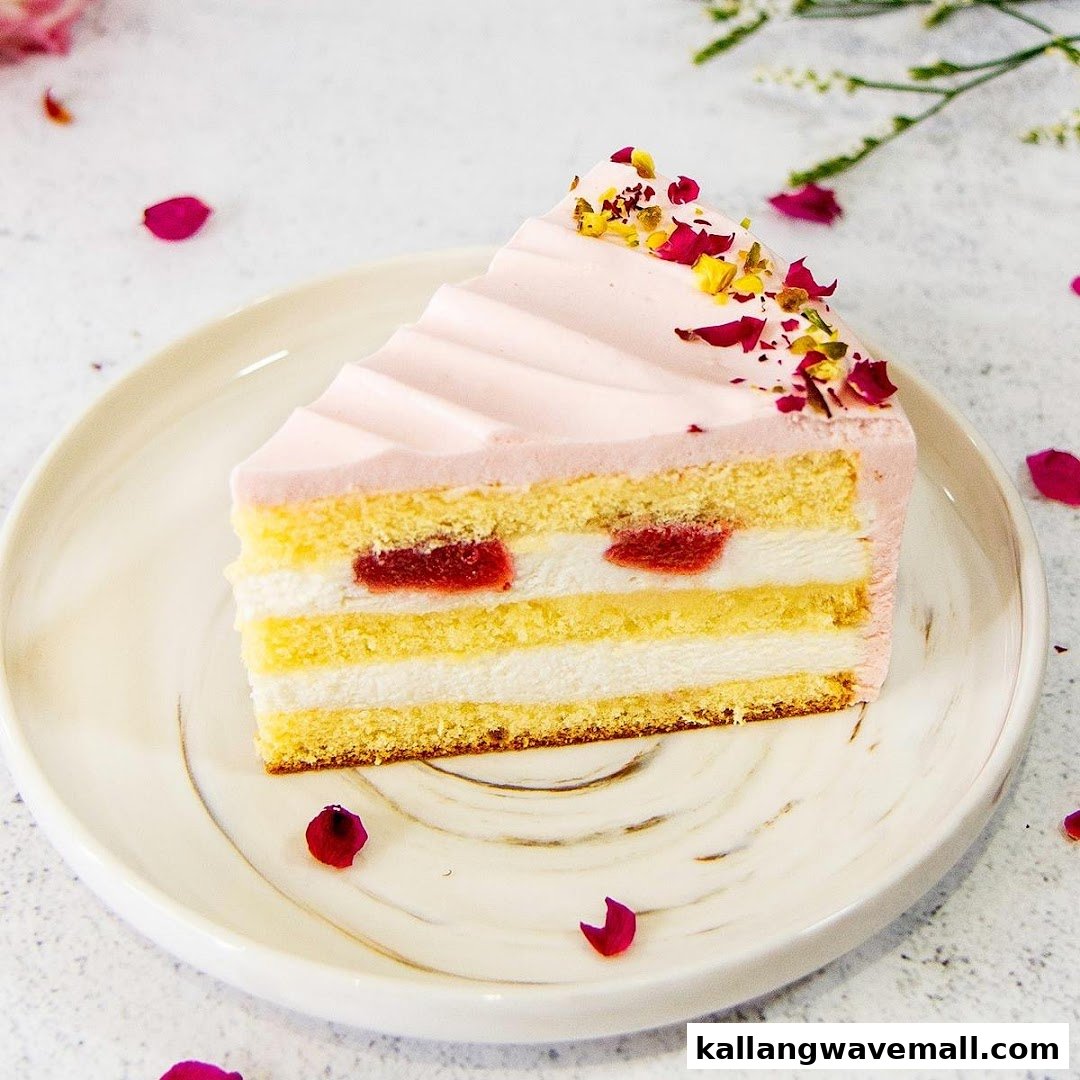 A delicious slice of layered cake with pink frosting, fruit filling, and floral garnish on a white plate.