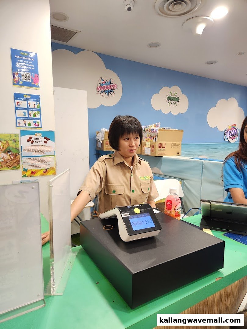 An employee at the vibrant counter of Jolly Fields by Zoomoov, a children's activity center.