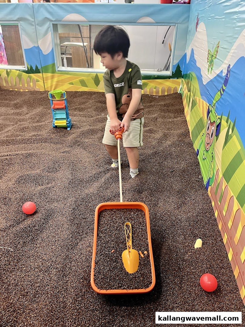 A young child plays with toys in a large indoor play area filled with dark pellets.