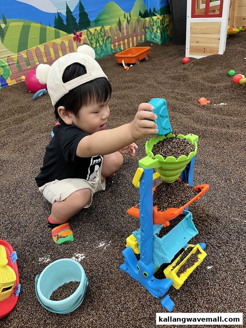 A young child plays with a toy and brown pellets in a vibrant indoor play area.