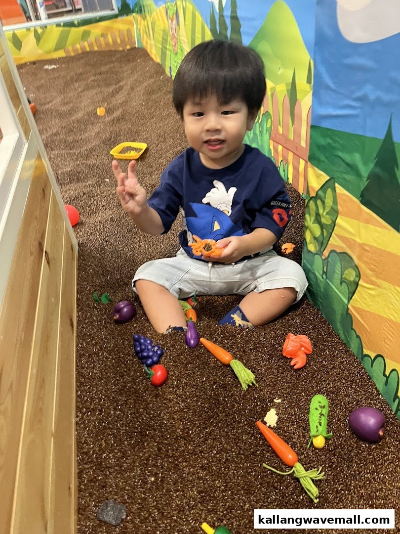 A happy child plays in a simulated farm pit with toy vegetables and fruits at Jolly Fields.