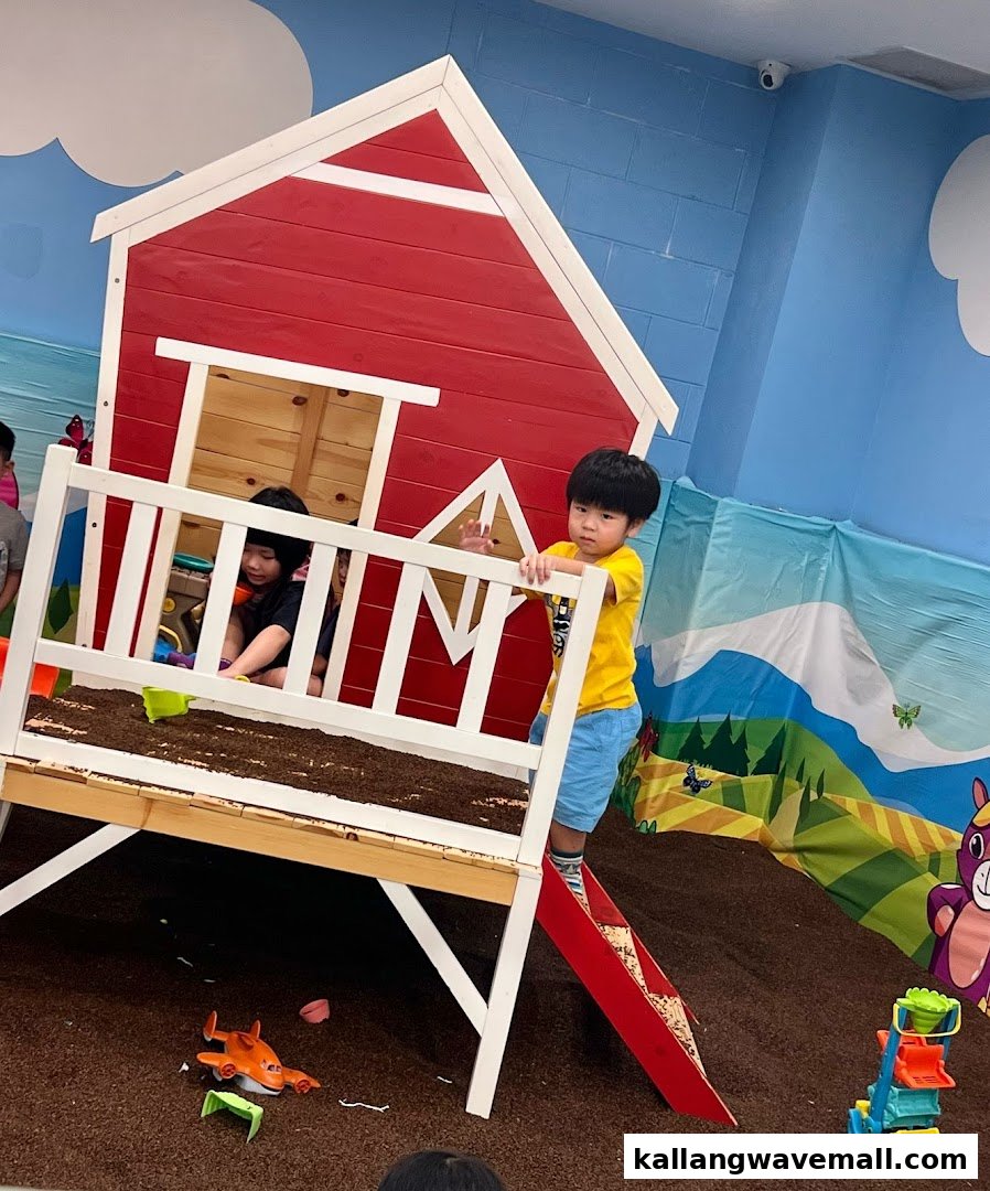 Children play in an indoor farm-themed soft play area with a red barn structure and various toys.