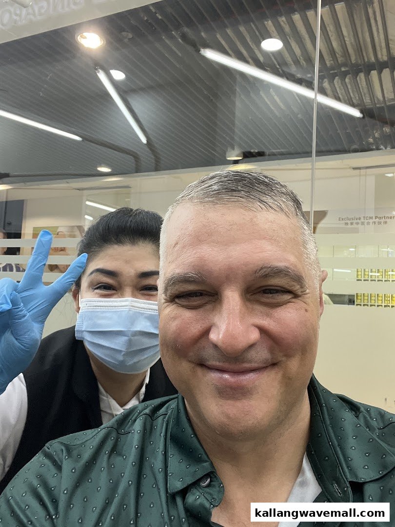 A smiling customer takes a selfie with a masked kcuts staff member giving a peace sign.