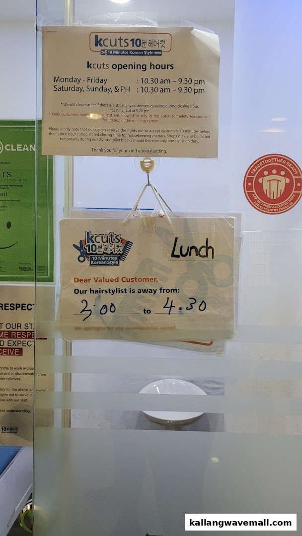 The image displays the entrance of kcuts, a hair salon, with signs detailing opening hours and a temporary lunch break notice.