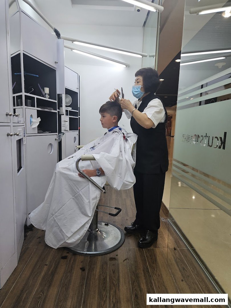 A young boy receives a haircut from a masked stylist inside a Kcuts salon.