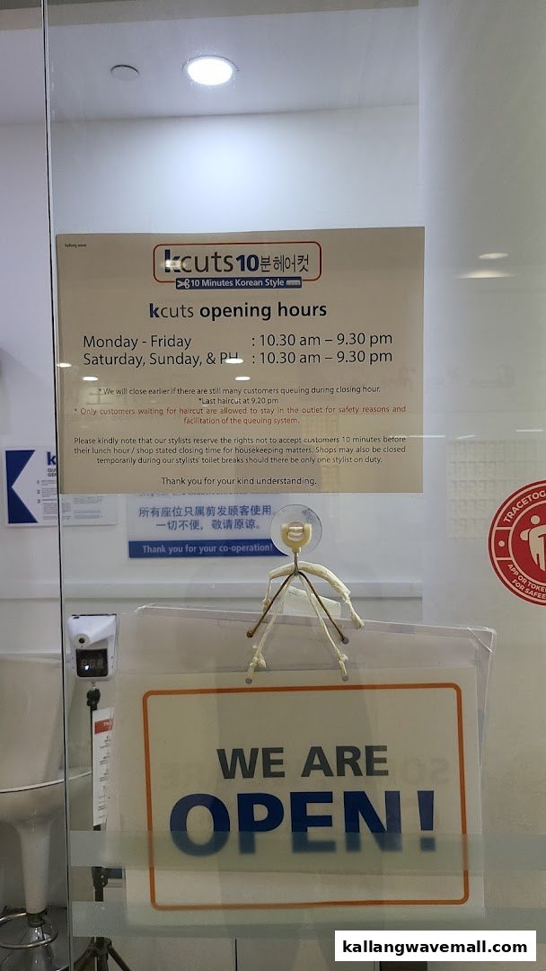 The entrance of kcuts Kallang Wave Mall, displaying opening hours and an 'OPEN' sign.