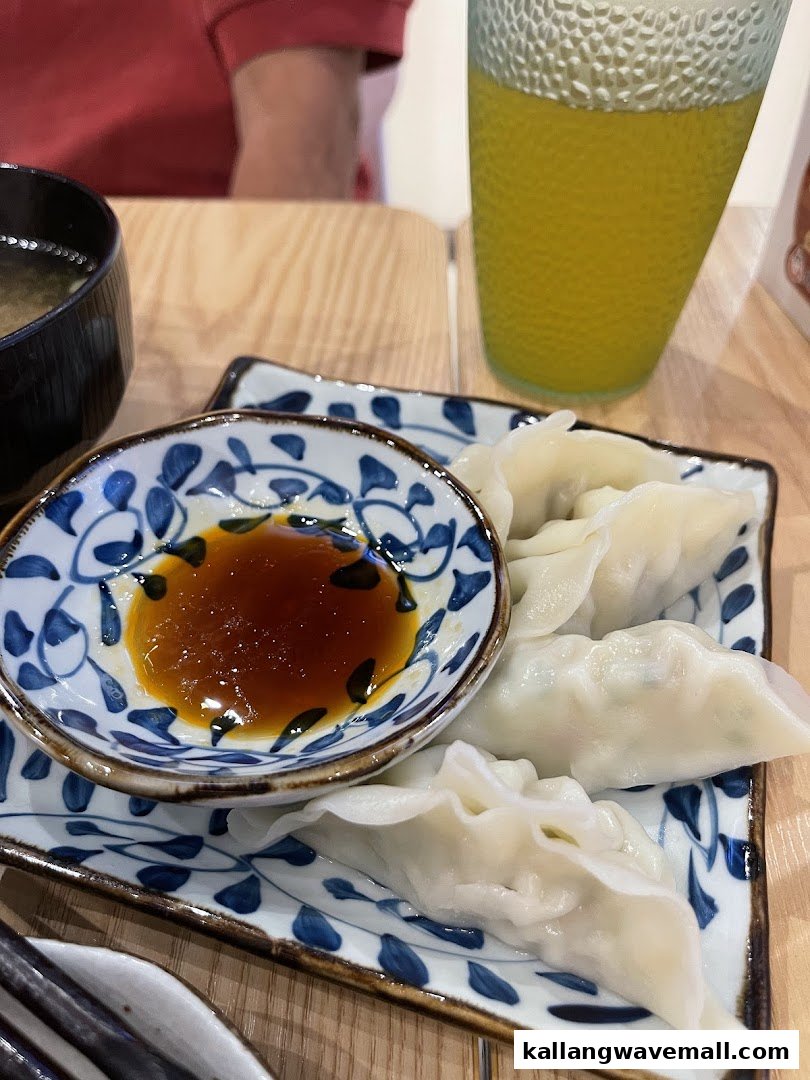 A plate of steamed dumplings with dipping sauce, miso soup, and a drink on a wooden table.