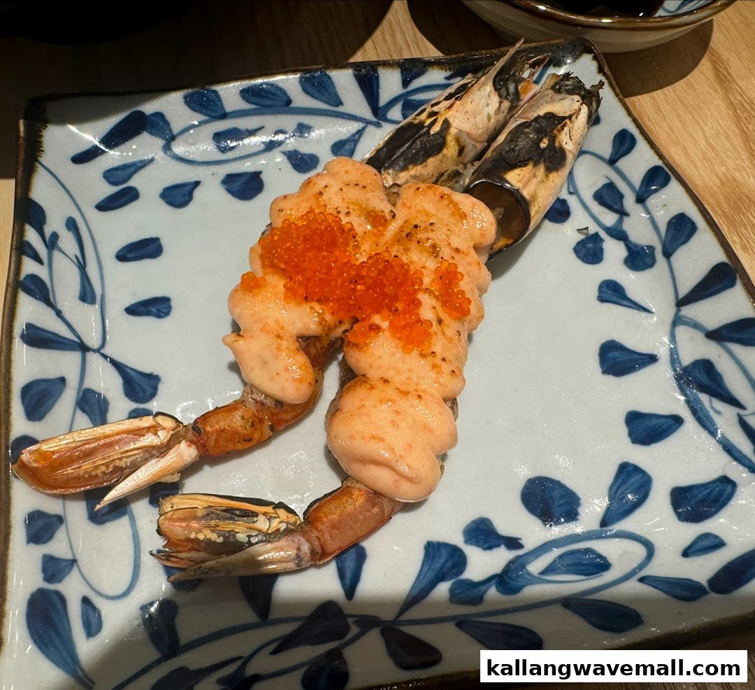 Two grilled prawns topped with creamy sauce and bright orange roe on a decorative plate.