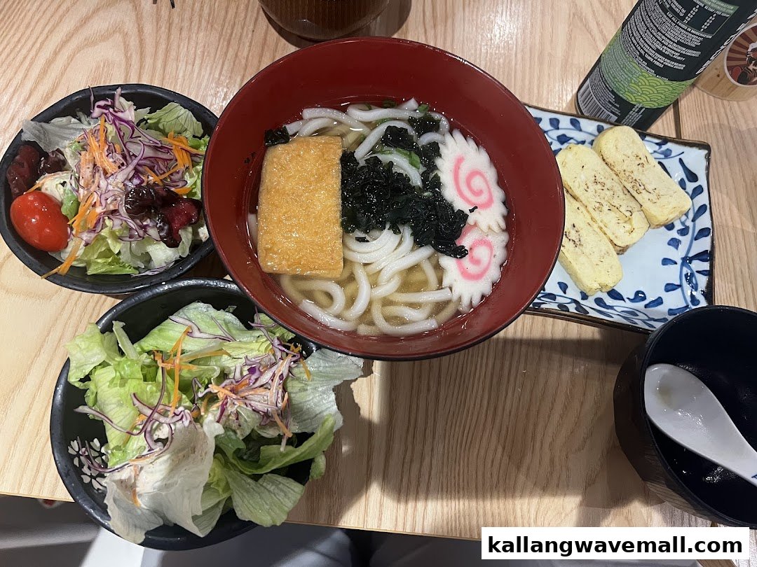 A delicious Japanese meal featuring udon, fresh salads, and tamagoyaki on a wooden table.