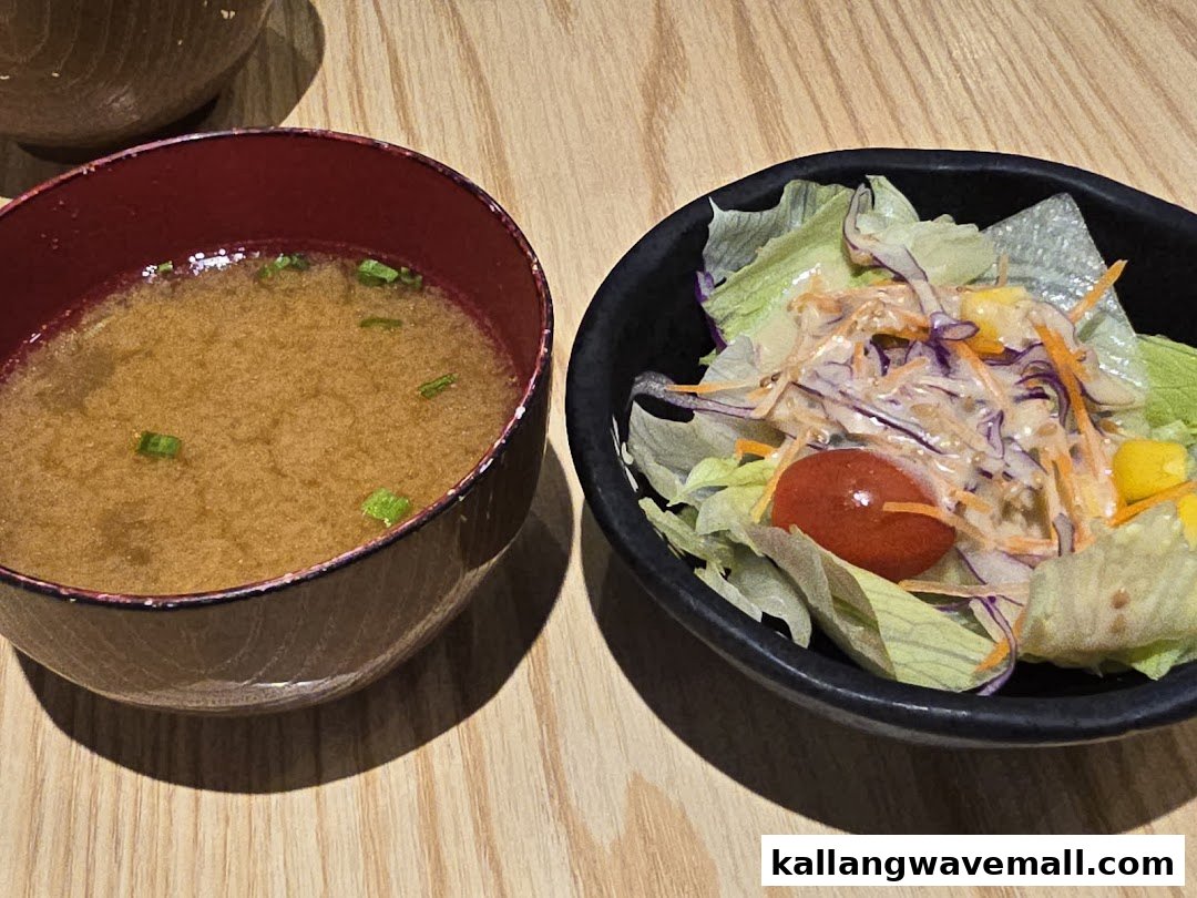 A comforting bowl of miso soup and a fresh side salad on a wooden table.