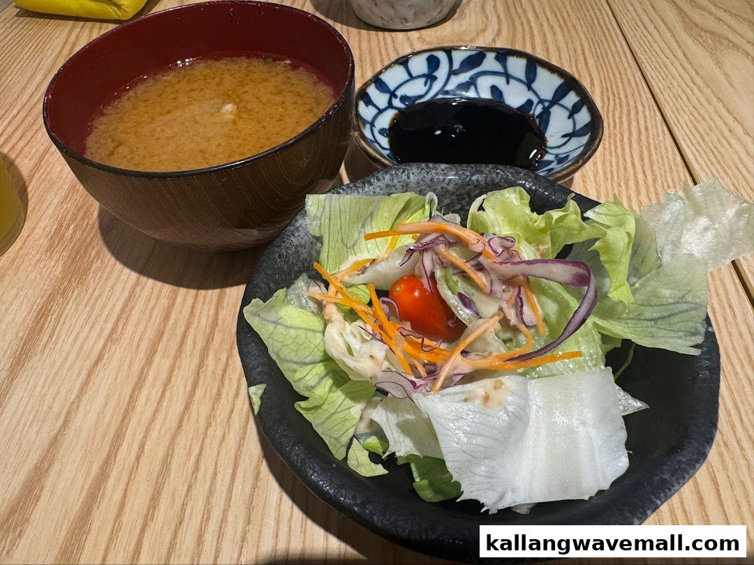 A close-up of a fresh side salad, miso soup, and soy sauce on a wooden table.