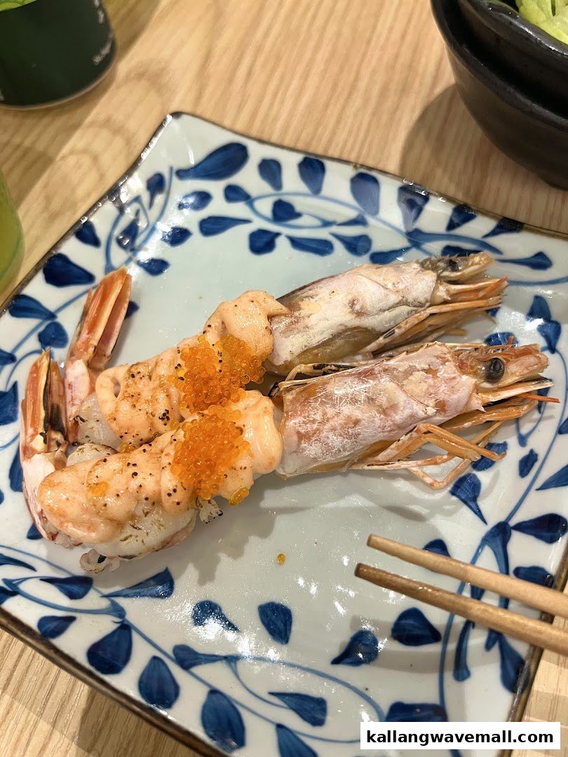 Two pieces of grilled shrimp sushi topped with orange roe on a decorative plate with chopsticks.
