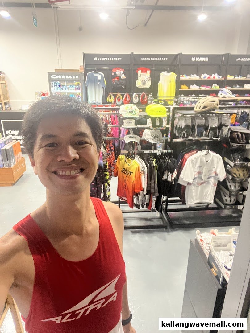 A smiling person in a sports shop, surrounded by athletic apparel, footwear, and gear.
