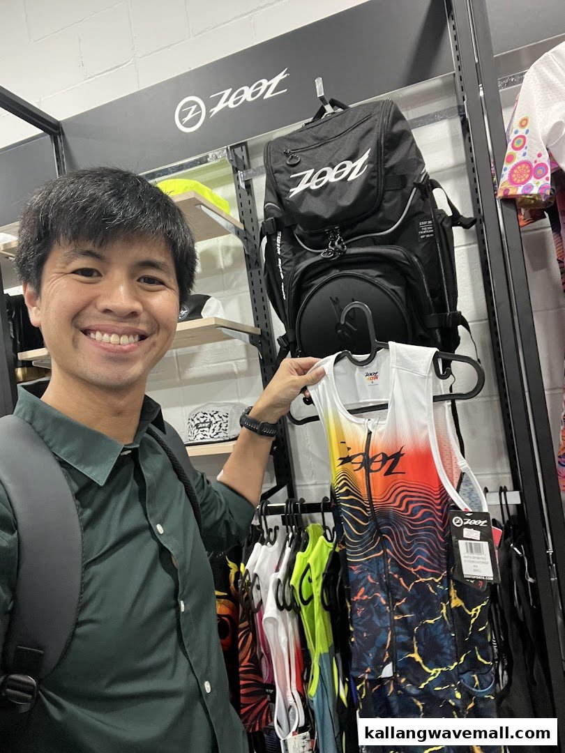 A smiling man holding a Zoot sports top in a retail store.