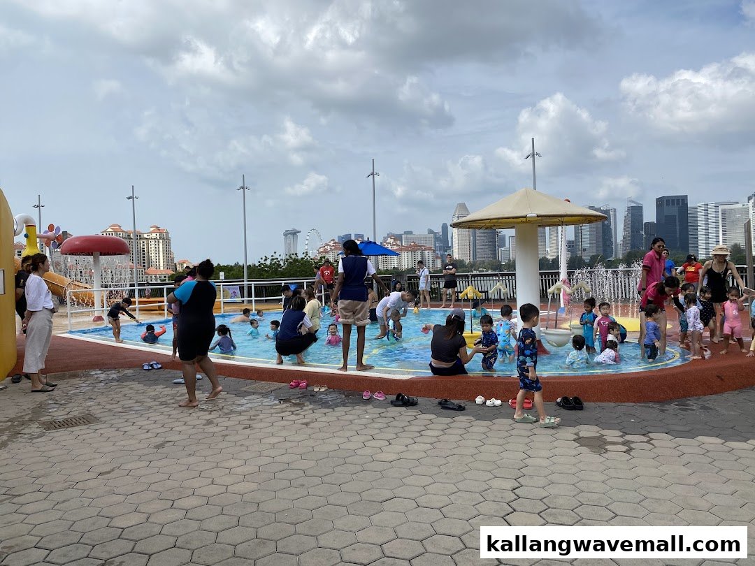 Children and adults enjoy a vibrant outdoor water play area with a city skyline backdrop.
