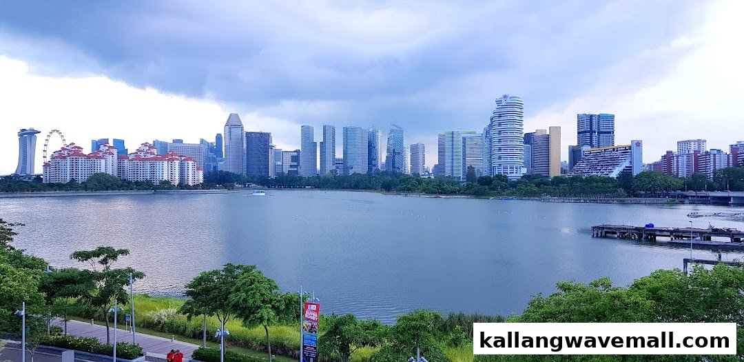 A panoramic view of a modern city skyline across a serene body of water under a cloudy sky.