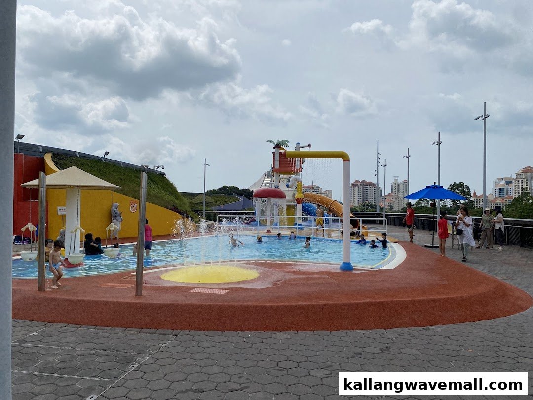 An outdoor water play area with children and adults enjoying various water features under a cloudy sky.