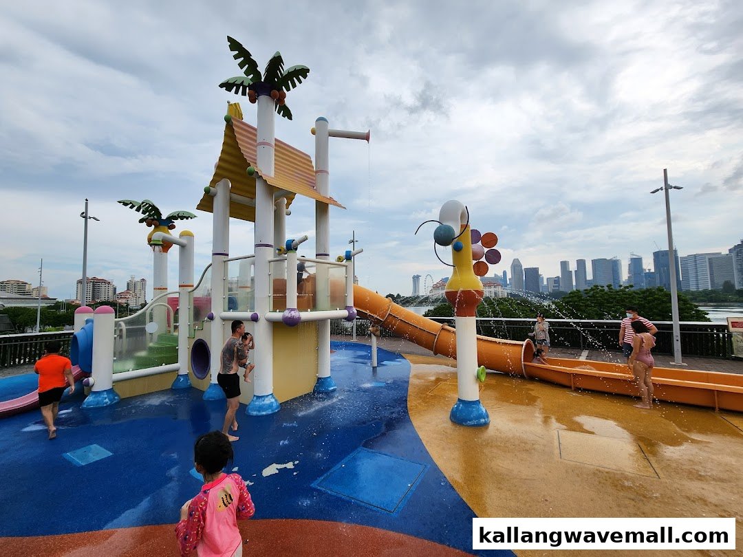 Children and adults enjoy a vibrant outdoor water play area with slides and sprayers under a cloudy sky.