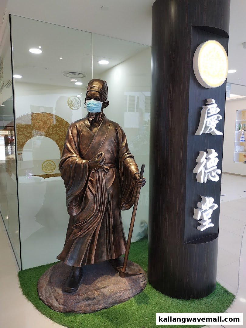 A masked bronze statue of a traditional Chinese physician stands at the entrance of Kin Teck Tong TCM Clinic.